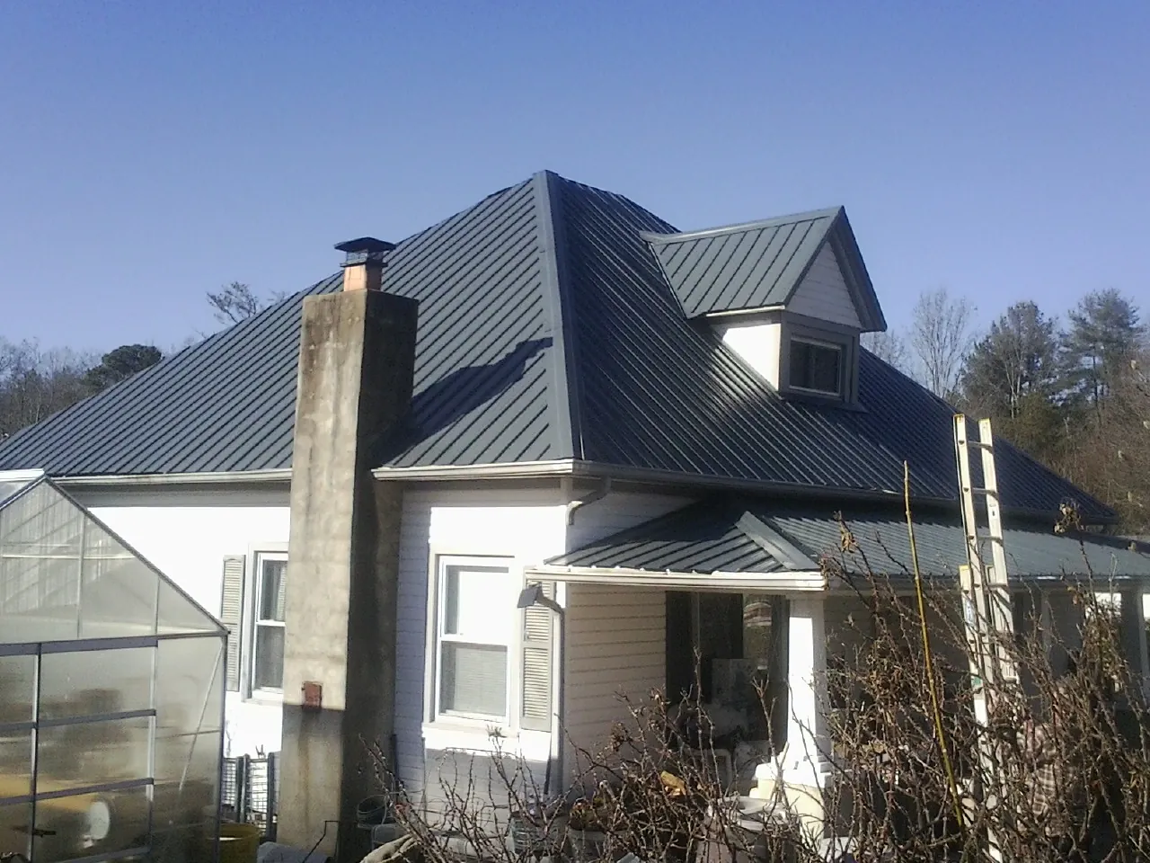 Dark blue standing seam metal roof on a white farmhouse with dormer — Slate & Tile Roof Repair by Roofing Brothers in Tingley