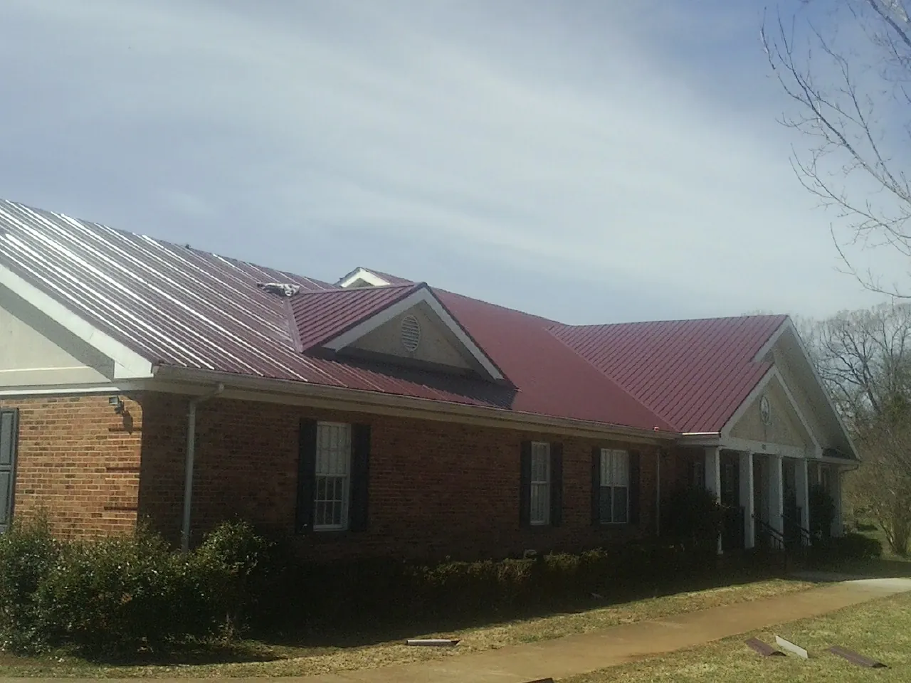 Red metal roof with gabled entries on a long brick building, from a Hail Damage Roof Repair job in Tingley
