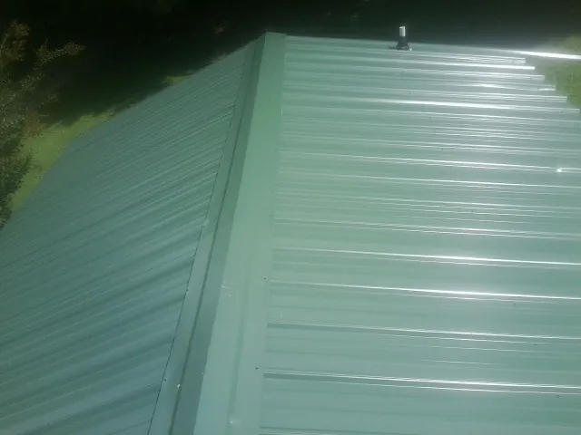 New green metal panels meeting at the ridge of a roof — Flat Roof Repair work by our crew in Tingley