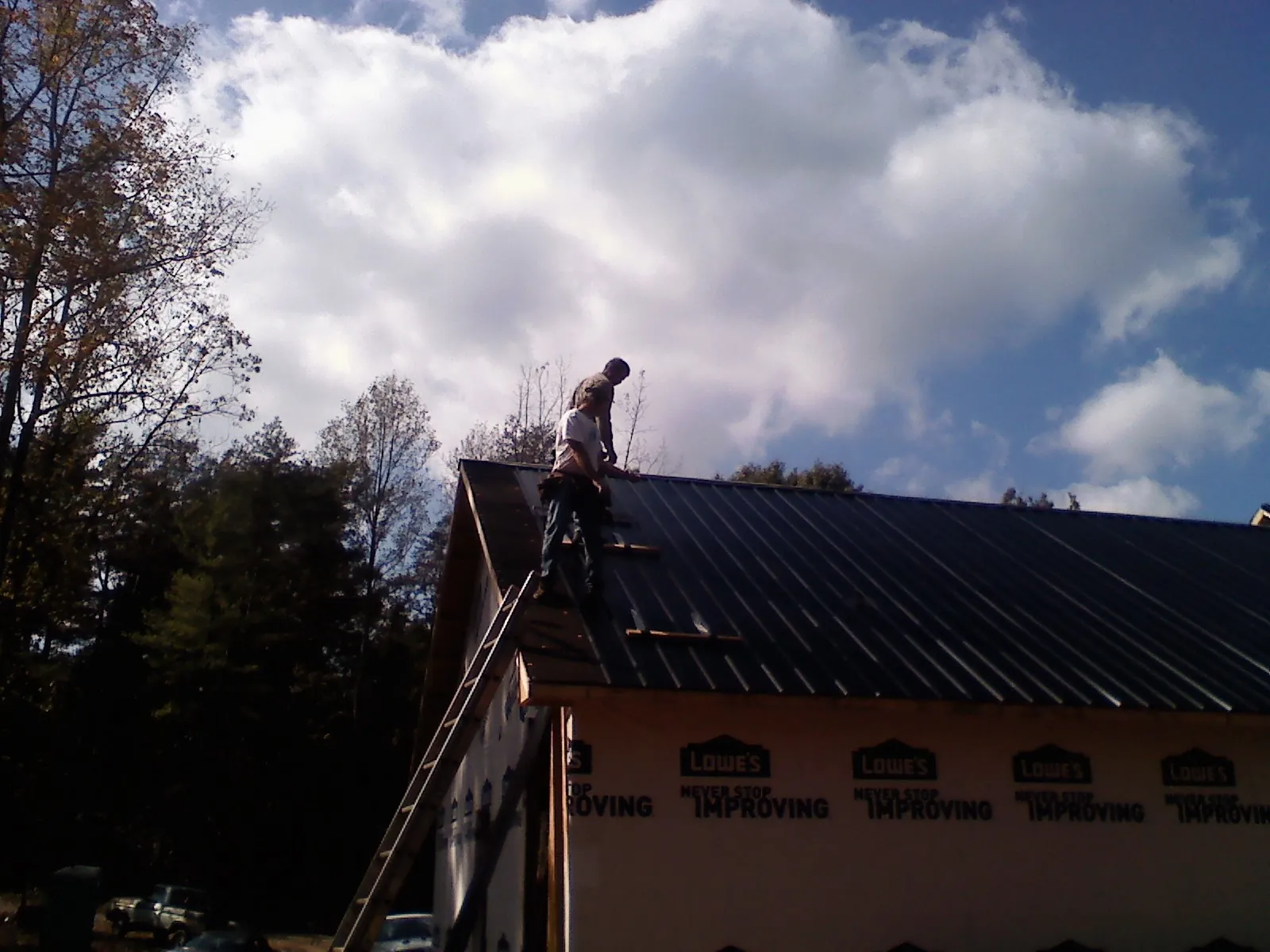 Roofer fastening dark metal panels high against a cloudy sky, from a Roof Inspection job in Tingley