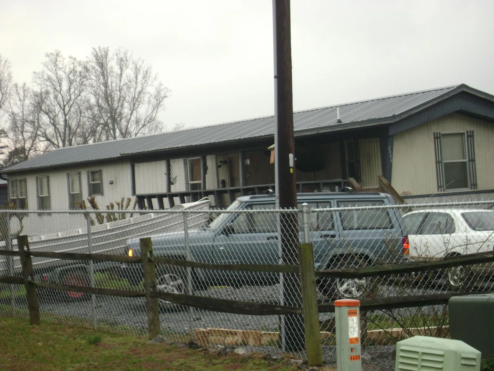 Dark metal roof on a long single story building behind a chain link fence in Tingley