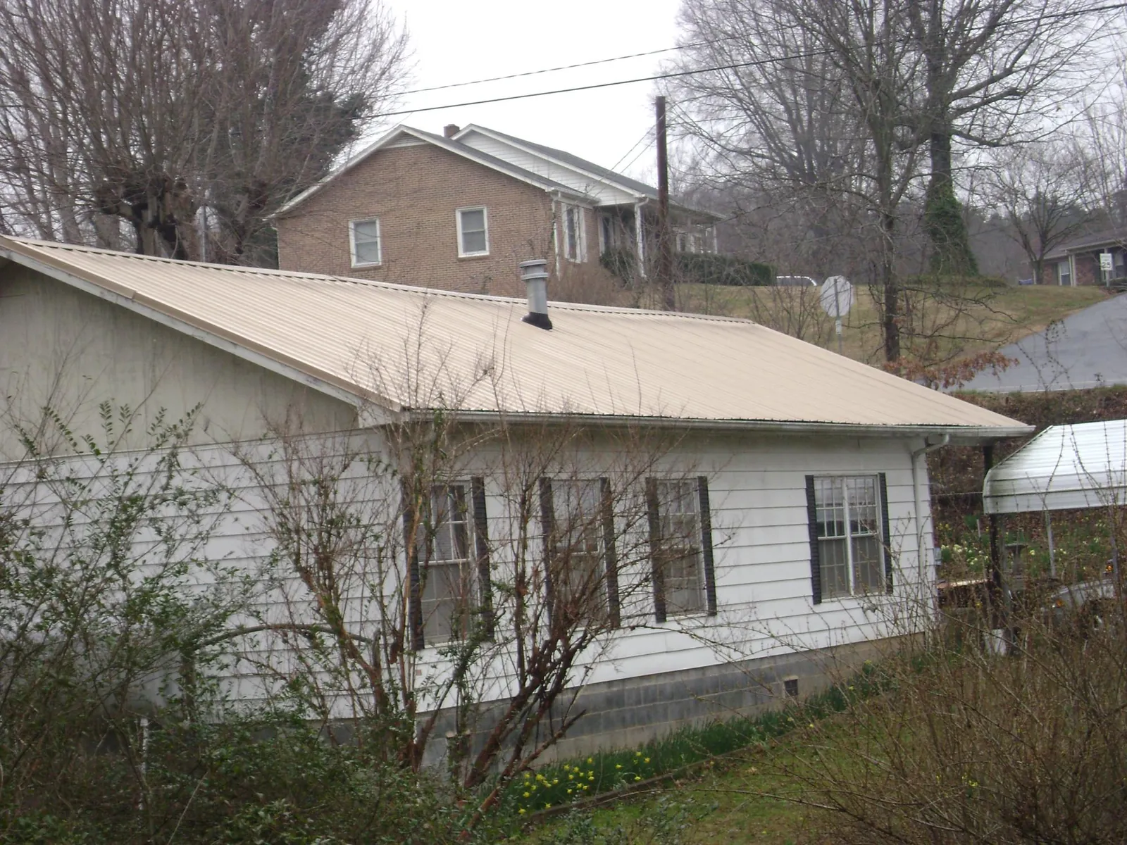 Tan metal roof on a white sided house set into a hillside — Commercial Roofing by Roofing Brothers in Tingley